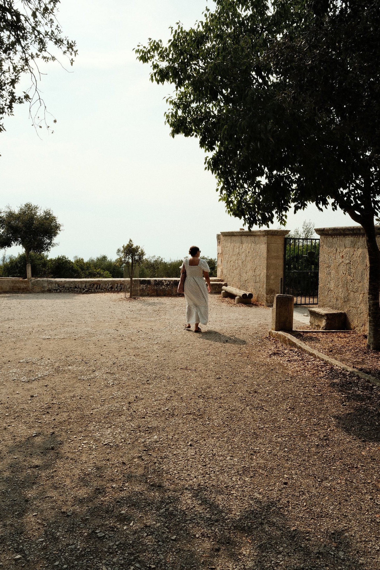 Woman in white walking near a stone wall